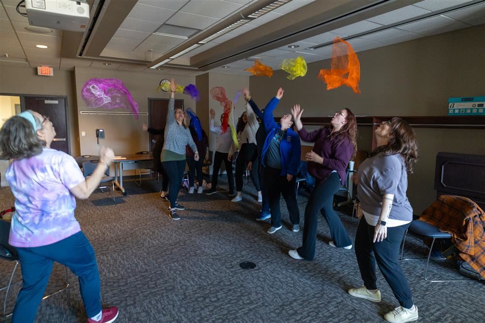  A group of educators are practicing an exercise for their students by throwing fabric in the air.